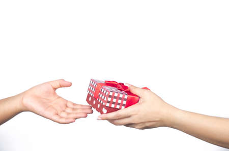 Closeup hands giving and receiving Christmas gift box wrapped with red ribbon isolated on white backgroundの写真素材