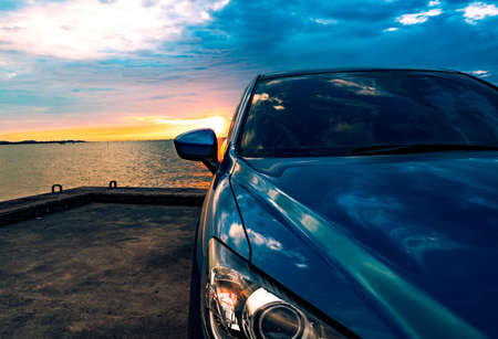 Blue compact SUV car with sport and modern design parked on concrete road by the sea at sunset. Environmentally friendly technology. Business success concept.の写真素材