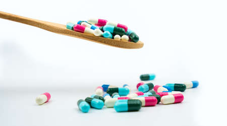 Colorful of antibiotics capsule pills in wooden spoon are spilling on white background with copy space. Antibiotic drug use with reasonable and health insurance concept.の写真素材