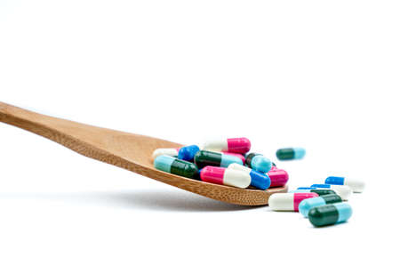 Colorful of antibiotics capsule pills in wooden spoon are spilling on white background with copy...