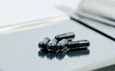 Selective focus on powders of activated charcoal on stainless steel drug tray and blur capsule...