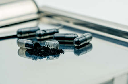 Selective focus on powders of activated charcoal on stainless steel drug tray and blur capsule backgroundの写真素材