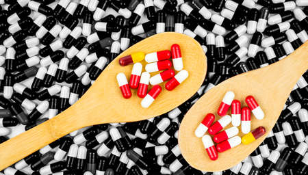 Colorful of antibiotics capsule pills in wooden spoon on black and white background of capsules. Drug resistance concept. Antibiotics drug use with reasonable and global healthcare concept.の写真素材