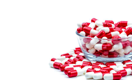 Red, white antibiotic capsules pills in glass bowl and some on white background with copy space. Drug resistance concept. Antibiotics drug use with reasonable and global healthcare concept.の写真素材