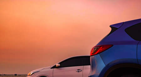 Blue compact SUV car with sport and modern design parked on concrete road by the sea at sunset. White Eco car. Environmentally friendly technology. Business success concept.の写真素材