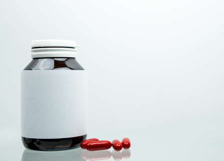 Macro shot of red multivitamins capsule pills for pregnant woman with amber bottle and blank label...