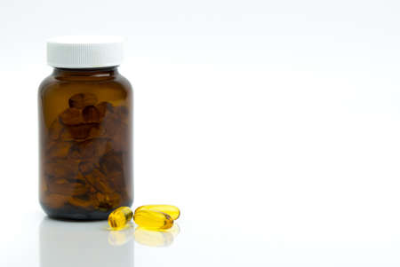 Yellow fish oil capsule pills with amber glass bottle with blank label on the table with copy space for text. Vitamins and supplements for heart care and joint care. Source of omega 3, EPA and DHA.の写真素材
