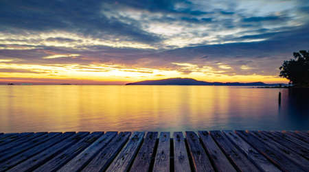 Wood pier with sea and mountain at sunrise with beautiful golden sky in the morning and copy space use as background to display goods and product.の写真素材