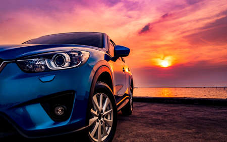 Blue compact SUV car with sport and modern design parked on concrete road by the sea at sunset. Environmentally friendly technology. Business success concept.の写真素材