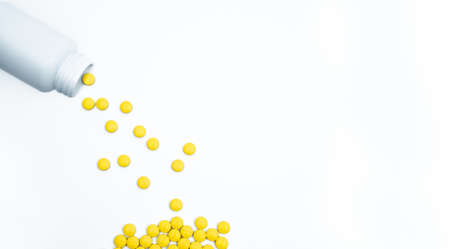 Yellow film coated tablets pills spilling out of pill bottle on white background with copy space. Painkiller tablet pills. NSAIDs pills for muscle pain.の写真素材