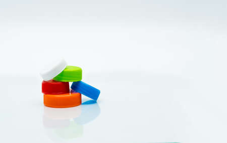 Pile of different size of white, green, red, blue and orange color round plastic screw caps on white...