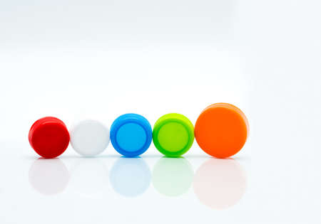 Different size of white, green, red, blue and orange color round plastic screw caps in a line on...