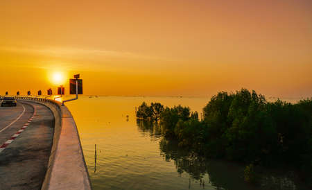 Curved coastal road and car with orange sky at sunset in Chonburi, Thailand.