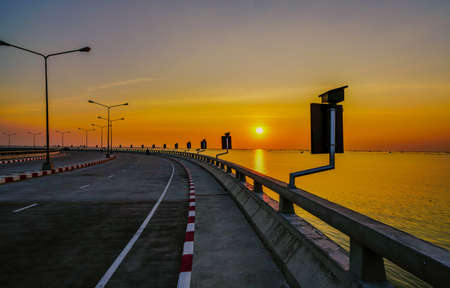 Curved coastal road with street lamp and orange sky at sunset in Chonburi, Thailand.の写真素材