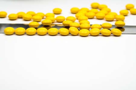 Macro shot detail of yellow round sugar coated tablets pills and stainless steel spatula on white background with copy spaceの写真素材