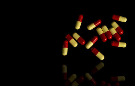 Red, yellow capsule pills on dark background. Antimicrobial resistance concept.の写真素材