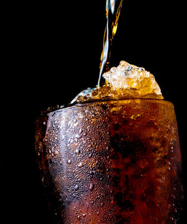 Soft drink pouring to glass with ice isolated on dark backgroundの写真素材
