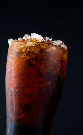 Soft drink with ice in glass isolated on dark background with copy space. There is a drop of water on the transparent glass surface.の写真素材