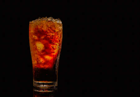 Soft drink with crushed ice cubes in glass isolated on dark background with copy space. There is a drop of water on the transparent glass surface.の写真素材