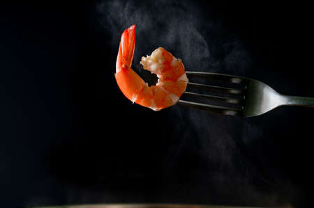 Steamed shrimp on fork isolated on dark background with copy space. Seafood buffet in restaurant concept. Use for seafood buffet promotions advertisingの写真素材