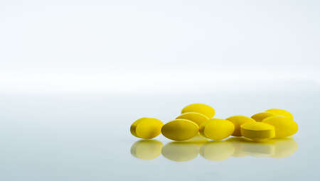 Pile of yellow oval tablet pills on white background with copy space for text. Mild to moderate pain management. Pain killer medicine. Medicine for relieve high fever.の写真素材