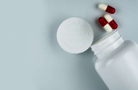 Capsules pills on white background and plastic bottle with blank label and copy space. Childproof packaging. Child resistant pill container. Push down and turn cap. Global healthcare concept.の写真素材