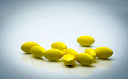 Yellow oval tablet pills with shadows on white background with beautiful creative pattern and copy space for text. Mild to moderate pain management. Pain killer medicine.の写真素材