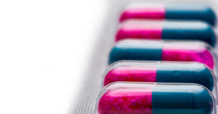 Selective focus of blue, pink capsule with granule in side pills. Pills in blister pack on white background. Pharmaceutical dosage form and packaging. Itraconazole 100 mg : Anti-fungal medicine.の写真素材