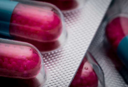 Selective focus of blue, pink capsule with granule in side pills. Pills in blister pack on white background. Pharmaceutical dosage form and packaging. Anti-fungal medicine.の写真素材