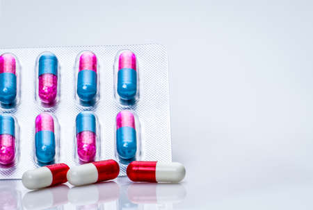 Red-white antibiotic capsule pills and pink-blue anti-fungal granules in capsule pills in blister pack on white background Antibiotics drug resistance and antimicrobial drug use with reasonable.の写真素材