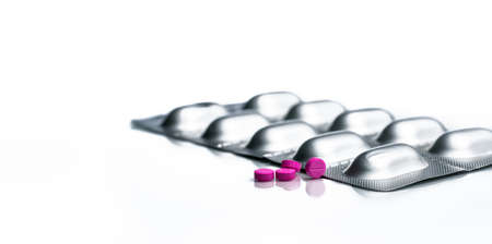 Small pink tablets pills and aluminium foil blister pack of pills isolated on white background with...