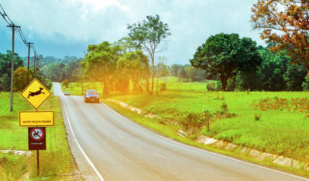 Blue SUV car of the tourist driving with caution during travel at asphalt road near yellow traffic sign with deer jumping inside the sign and have message caution wildlife crossing. No feed wildlifeの写真素材