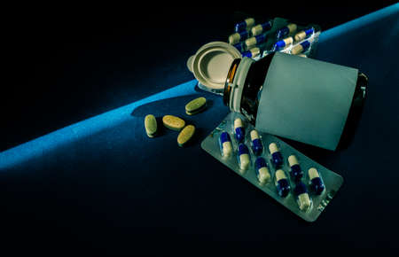 Pills and opened cap medicine bottle with blank label on dark blue background with copy space. Tablets and capsules. Pharmaceuticals industry. Vitamins and supplements.の写真素材