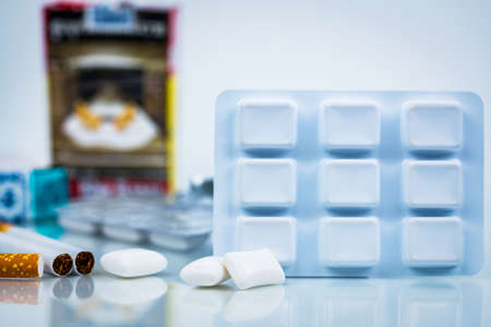Nicotine chewing gum in blister pack on blurred background of cigarette pack.  Medicine for giving...