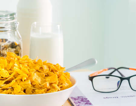 Bowl of cereal with spoon and one glass of milk put on wood table near diabetes textbook and eyeglasses. Calcium food breakfast . Cornflakes and milk conceptの写真素材