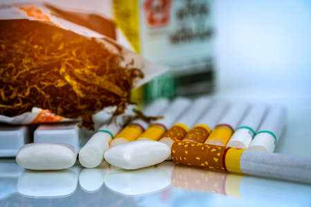 Nicotine chewing gum near pile of cigarettes and tobacco on white background with space. Quit...