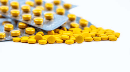 Selective focus on yellow tablets pills on blurred background of blister pack of round yellow pills....