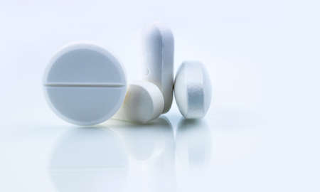 Pile of white round and oblong shape tablet pills isolated on white background. Pharmaceutical...