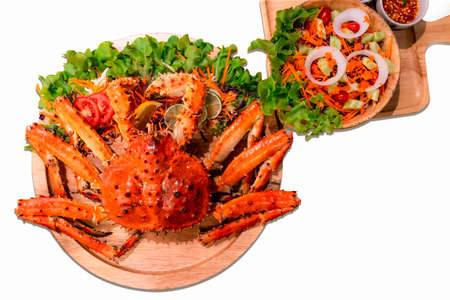 Cooked Alaskan king crab served with vegetable salad isolated on white background. Red Alaskan king crab legs on vintage wooden plate background. Seafood for lunch or luxury dinner.の写真素材