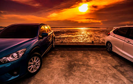 Blue and white compact SUV car with sport and modern design parked on concrete road by the sea at sunset. Environmentally friendly technology. Business success concept. Two carsの写真素材