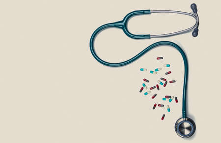 Green stethoscope with pile of capsule pills isolated on white background with copy space. Medical tool for doctor. Health check up concept. Medical equipment. Clinical Cardiology concept.の写真素材