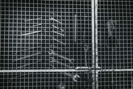 Unlocked mechanic tool cabinet made of metal net. Wrench arranged neatly in tool cabinet. Set of silver wrench and air gun hanging on black wood in workshop. Technician equipment. Handyman concept.の写真素材