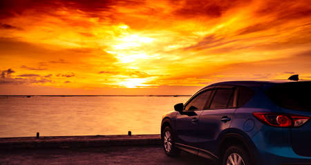 Blue compact SUV car with sport and modern design parked on concrete road by the sea at sunset. Hybrid auto and automotive concept. Road trip and car driving for travel. Car parked near the beach.の写真素材