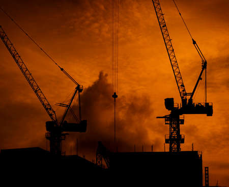 Construction cranes on high-rise building with dramatic orange sky and clouds at sunset time in the evening. Construction site of commercial building or condominium in city. Architecture background.の写真素材