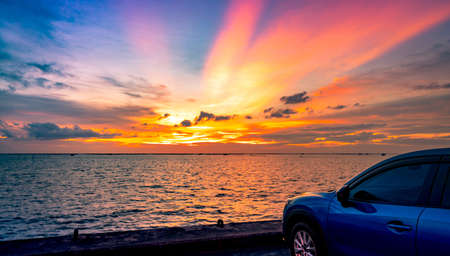 Blue compact SUV car with sport and modern design parked on concrete road by the sea at sunset. Road trip travel. Electric car technology and business. Hybrid auto and automotive industry concept.の写真素材