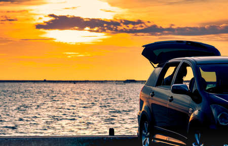 Silhouette SUV car with sport and modern design parked on concrete road by the sea at sunset. Road trip travel on vacation at the beach and open car truck with beautiful orange sunset sky and clouds.のeditorial素材