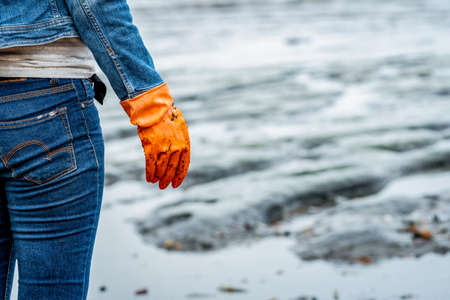 Volunteers wear jeans and long sleeved shirts and wear orange rubber gloves to collect garbage on the beach. Beach environment. Woman cleaning the beach. Tidying up rubbish on beach.の写真素材