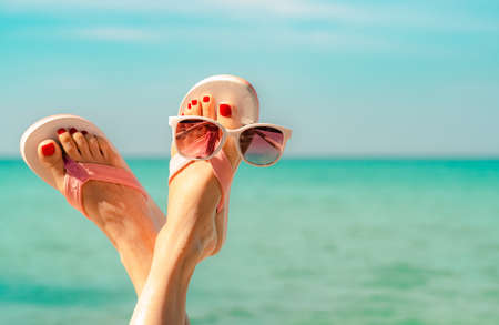 Upside woman feet and red pedicure wearing pink sandals, sunglasses at seaside. Funny and happy fashion young woman relax on vacation. Chill out girl at beach. Creative for tour agent. Weekend travel.の写真素材