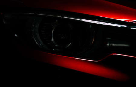 Closeup headlight of shiny red luxury SUV compact car. Elegant electric car technology and business concept. Hybrid auto and automotive concept. Car parked in showroom or motor show. Car dealership.の写真素材