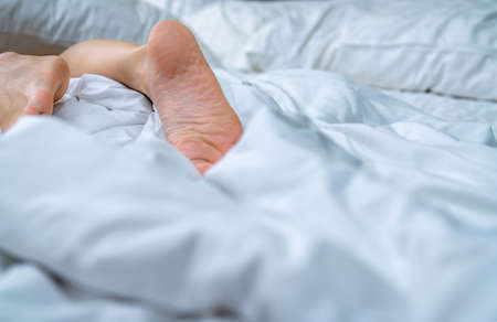 Close up woman bare feet on the bed  over white blanket and bed sheet in the bedroom of home or hotel. Sleeping and relax concept. Lazy morning. Barefoot of woman lying on white comfort bed and duvet.の写真素材